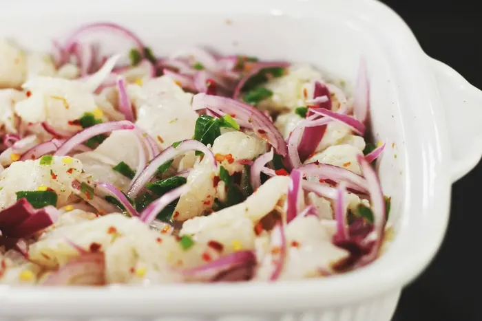 Fish ceviche with sliced red onion and herbs in a white baking dish