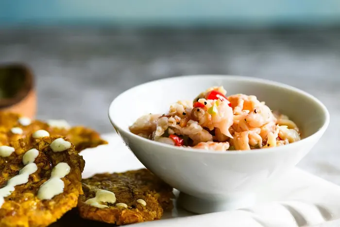 Shrimp ceviche in a white bowl beside fried tostones dotted with a pale sauce